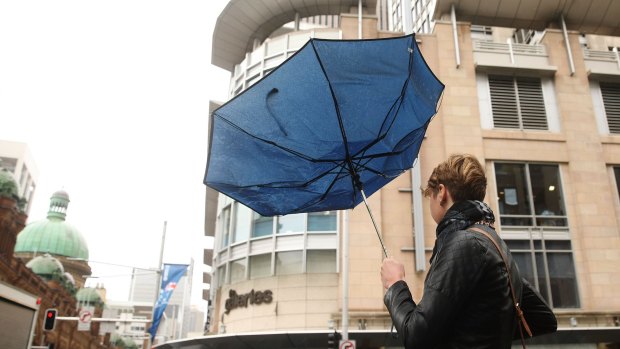 A woman walks in the CBD with a broken umbrella.