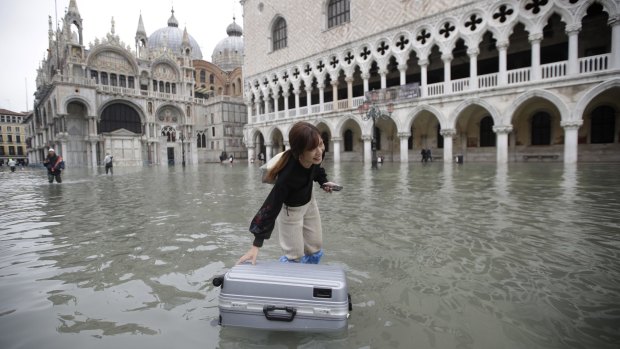 A tourist pushes her floating luggage in a flooded St. Mark's Square.