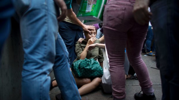 Irama Carrero is aided by fellow shoppers after fainting in a food line outside a grocery store, in Caracas. She said she hadn't eaten that day.