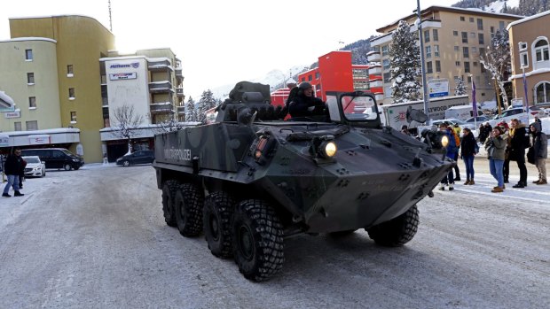 Pedestrian watch as an armoured Swiss military police vehicle drives past Davos Dorf railway station ahead of the World Economic Forum.