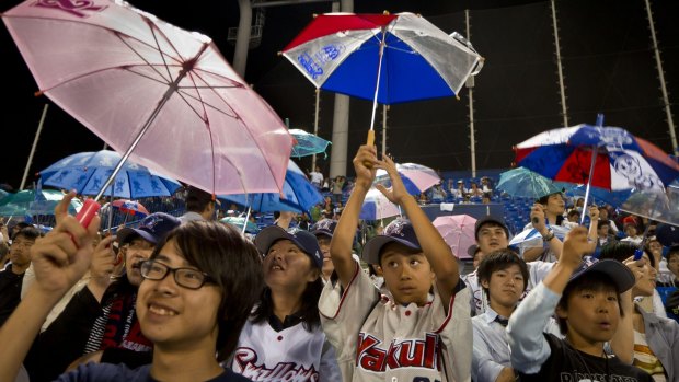 Fans of the Yakult Swallows Japan League baseball team sing and hold umbrellas overhead when one of their team's players hits a home run at Jingu Stadium.