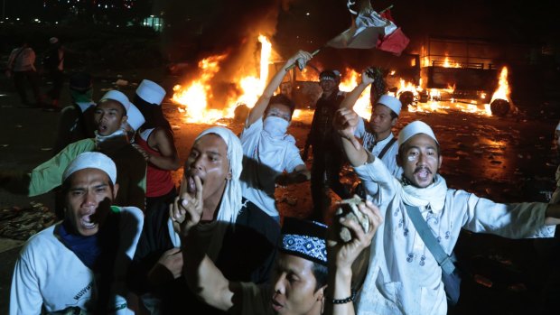 Muslim protesters chant slogans near burning police trucks.