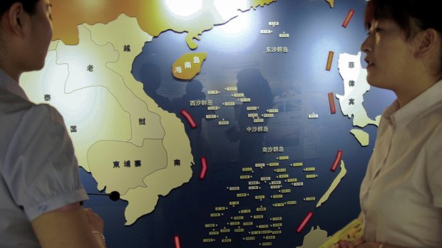 Workers chat near a map of South China Sea on display at a maritime defence educational facility in Nanjing, showing the nine-dash line claiming most of the area for China. 