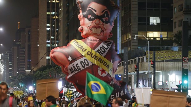 People protest next to a large inflatable Rousseff doll wearing a presidential sash saying "Goodbye dear" and "Mother of Big Oil", in Sao Paulo, on Monday.