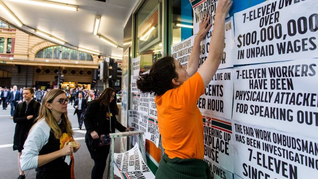 Protestors from the Young Workers Centre pin signs to the windows of 7-Eleven on the corner of Elizabeth and Flinders Street in Melbourne.