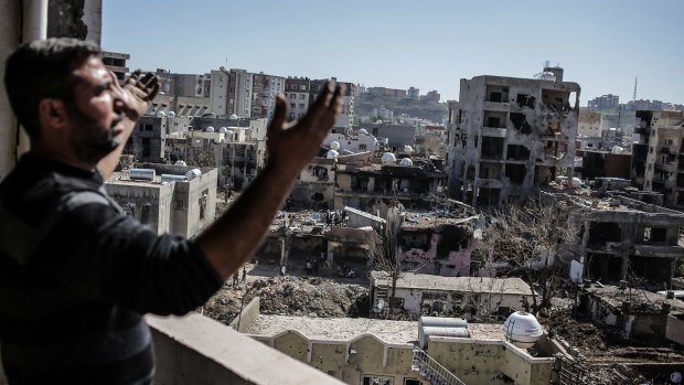 A man gestures as he looks at the ruined houses after returning to Cizre.