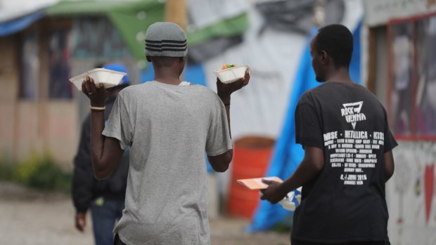 Migrants carry food outside the Jungle Books Cafe in the Jungle migrant camp on Tuesday.