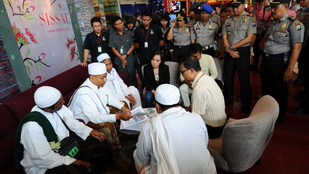 Police look on at a Surabaya shopping centre as centre staff sign a document promising not to dress employees in Christmas apparel.