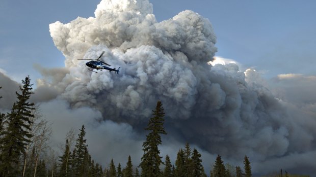 A helicopter flies past a wildfire in Fort McMurray, Canada