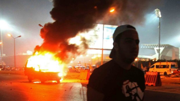 
A Zamalek fan near a police car, which was set on fire during clashes between football fans and security forces in front of a stadium on the outskirts of Cairo.