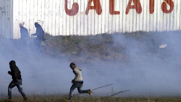Migrants run away from tear gas thrown by police forces near the Channel Tunnel in Calais, ahead of attempts to raze the camp on Thursday.
