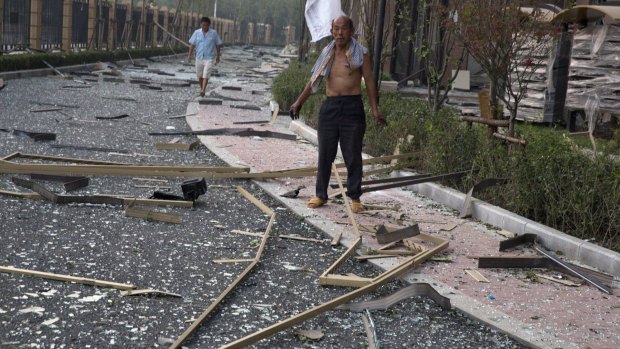 A man stands near broken glasses after the nearby explosion shattered windows at a residential compound, in Tianjin.