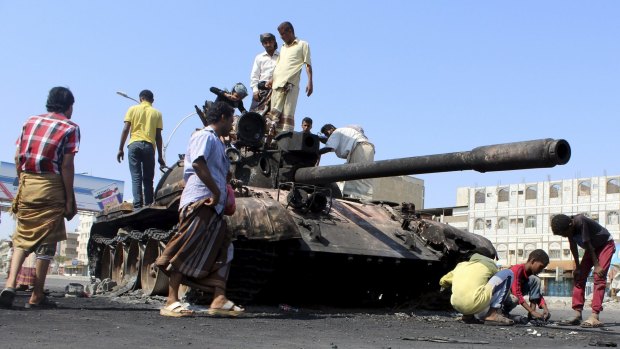 People gather near a tank burnt during clashes on a street in Aden, Yemen, on Sunday. 