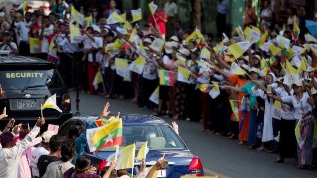 Pope Francis waves from the car as Catholic devotees wave flags welcoming him to Yangon, Myanmar. 