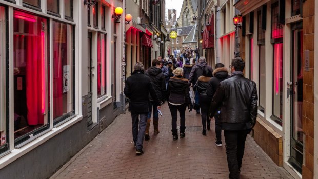 Tourists walking in the red light district of Amsterdam, where prostitutes try to lure customers from behind their window.