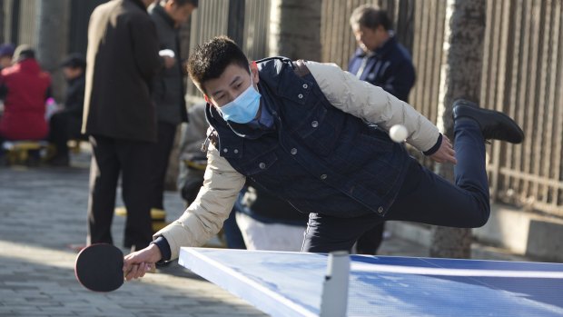A Chinese man wears a mask as he plays table tennis or ping pong at a park in Beijing, China. Chinese consumers are turning to an unusual tactic: buying cans of clean air from Canada.