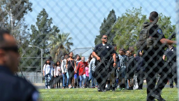 A San Bernardino police officer guides students on to the playground as multiple law enforcement agencies respond to a shooting.