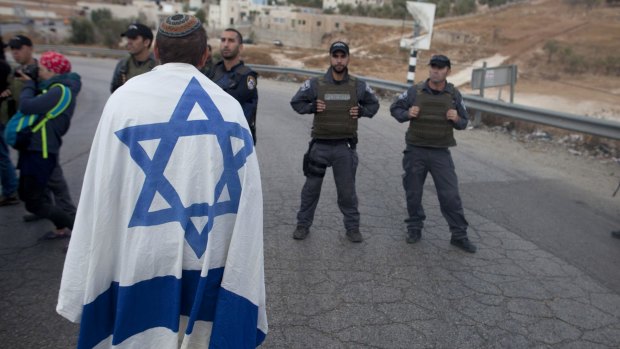 An Israeli settler draped in the country's flag stands next to Israeli police in a demonstration at the enterance to the  Palestinian village of Beit Sahur, in the occupied West Bank. 