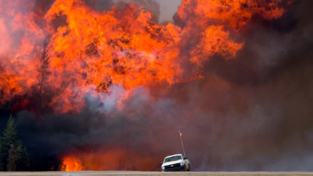 A wildfire burns behind an abandoned truck on Alberta Highway 63 near Fort McMurray on Saturday.