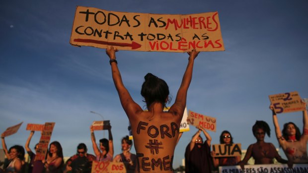 A woman with her body painted with the Portuguese message "Get out Temer" referring to Brazil's President, holds up a sign saying: "All women against all violence" in Brasilia.