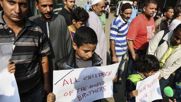 Egyptian boys hold posters to share sorrow outside Zeinhom morgue in Cairo