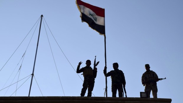 Iraqi soldiers plant the national flag over a government building in Ramadi.