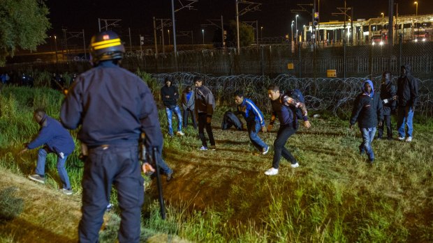 A policeman watches men move away from a security fence beside train tracks near the Eurotunnel terminal.