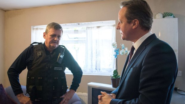 British Prime Minister David Cameron speaks with Immigration Enforcement officer John Keane in the house where three people were arrested earlier.
