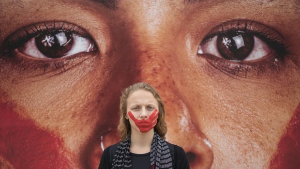 An activist poses for a photo in front of an installation on Copacabana beach portraying the anguish suffered by abused women.