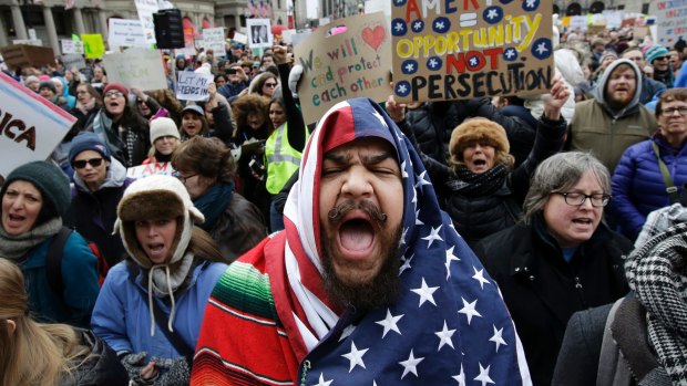 Izzy Berdan, centre, wears a US flag as he chants slogans with other demonstrators during a rally against President Donald Trump's travel in Boston.