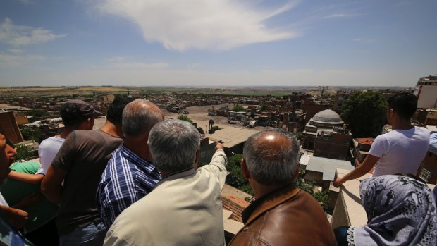 Diyarbakir residents on a nearby rooftop view damage to their city.