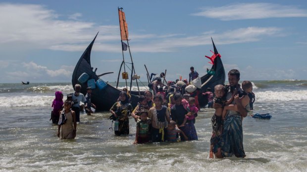 A Rohingya Muslim man walks to shore carrying two children in Bangladesh after they arrived on a boat from Myanmar  on Thursday.