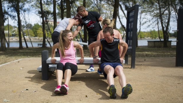 Bella Gay of TAMS and Shane Rattenbury in a group workout session at an older outdoor fitness station.