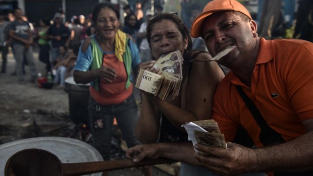 Demonstrators hold 100-bolivar banknotes while preparing food during the street protest in El Pinal.