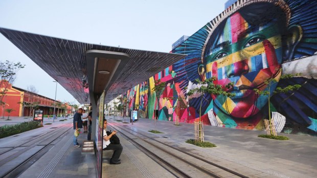 People wait for a tram next to the famed mural painted by artist Eduardo Kobra for the Rio 2016 Olympic Games in Rio de Janeiro.