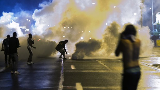 A protester throws back a smoke canister as police clear a street after a curfew imposed in the days after Michael Brown's death.