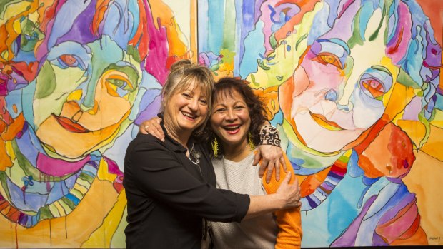 Childhood friends Beverley Pinder (left) and Rachel Rovay pose for a photo in front of a portrait of Beverley painted by Rachel for the Archibald competition.