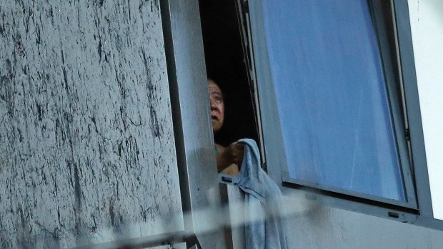 A resident peers out of a window from a small section of the building that was not on fire on Wednesday morning.