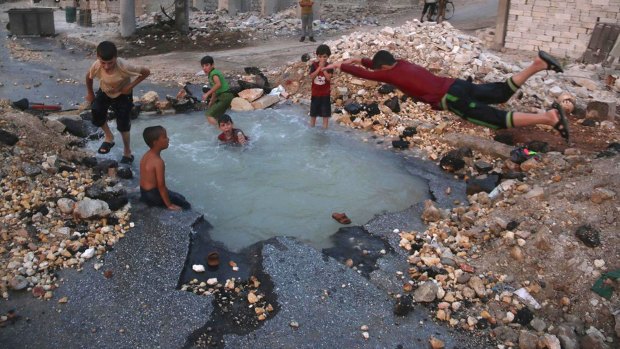 Syrian boys dive into a hole filled with water caused by a missile attack in Aleppo.