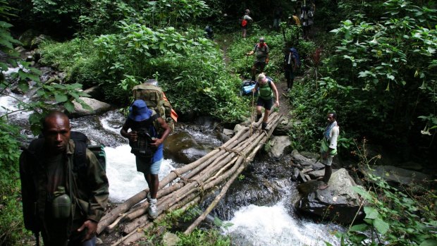 Trekkers cross the flowing river after a steep descent from the village called Alola while walking the Kokoda Track.