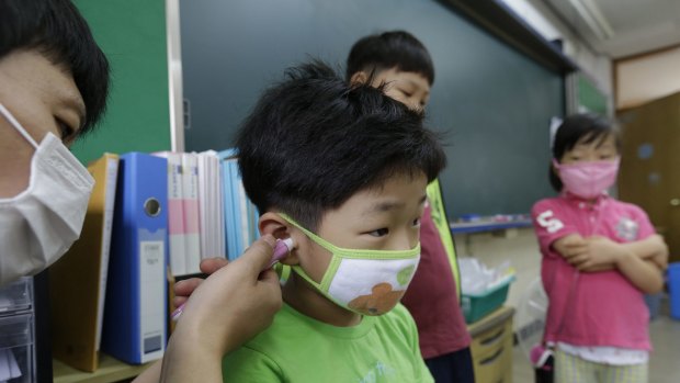 A teacher, left, checks the temperature of a pupil at Midlong Elementary School in Seoul.