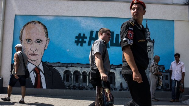 People walk by fresh graffiti depicting Russian President Vladimir Putin in Simferopol, Crimea.
