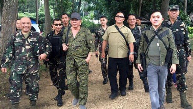 President Rodrigo Duterte, centre left, wearing a bullcap and an assault rifle slung on his shoulder, walks with  military officers   on the outskirts of Iligan city in the southern Philippines on Friday. Mr Duterte was supposed to fly to Marawi city but was forced to cancel  due to inclement weather. 