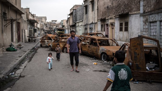 A man walks with his children past burnt out cars in a street in western Mosul, Iraq.