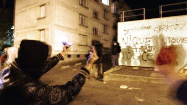 Youths gesture next to a wall with graffiti  that reads "F--- the police, Sarkozy resign", in the Renault housing complex of Les Mureaux, north-west of Paris, during the riots of 2005.
