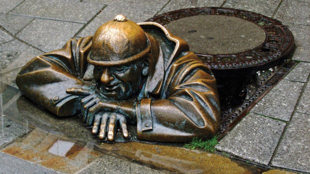 Offbeat bronze statue of a sewer worker resting at the top of a manhole, "peeping" at passersby.