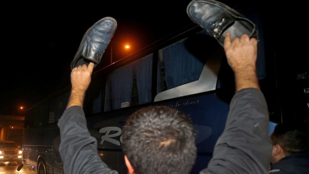 A Hezbollah supporter stands in front of a bus carrying Syrian opposition fighters, waving his shoes as an insult to them, upon their arrival at Rafik Hariri International Airport, in Beirut, Lebanon, on Monday.