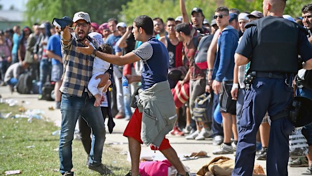 Migrants gesture and shout as they wait to board buses at Tovarnik train station.