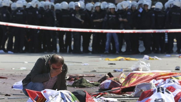 A man weeps over the body of a victim at the blast site as police look on.