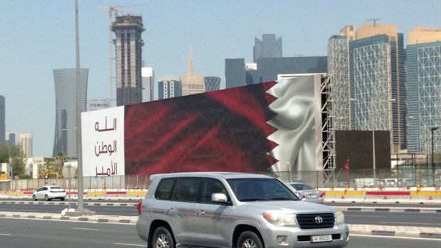 A Qatari SUV drives past a billboard featuring the Qatari flag and the slogan "God, Nation, Emir" in Doha, Qatar, on Monday.